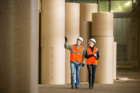 two people in high vis clothing walking through a papermaking facility paper industry
